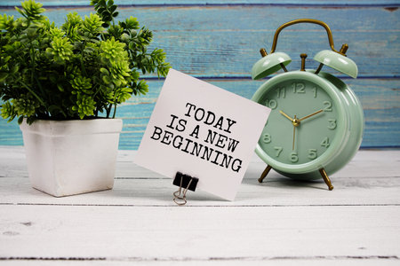 Today is a new beginning  text written on paper card with alarm clock on wooden backgroundの写真素材