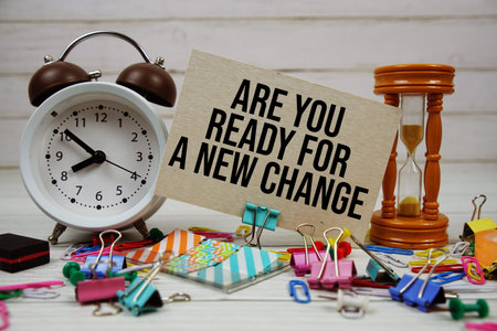 Are You Ready For A New Change? text on paper card with alarm clock and stationary on wooden...