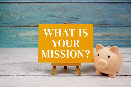 What is your mission? text written on paper card with piggy bank on wooden backgroundの写真素材