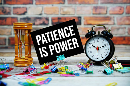 Patience Is Power text on paper card with alarm clock and stationary on wooden backgroundの写真素材