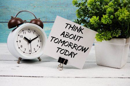 Think about tomorrow today  text written on paper card with alarm clock on wooden backgroundの写真素材