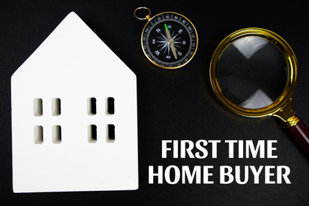 First Time Home Buyer text message with white house model and magnifying glass top view on black backgroundの写真素材