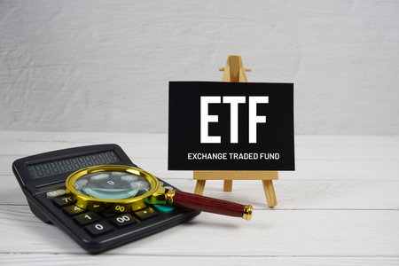 ETF abbreviation of Exchange Traded Fund text with magnifying glass and calculator on wooden backgroundの写真素材