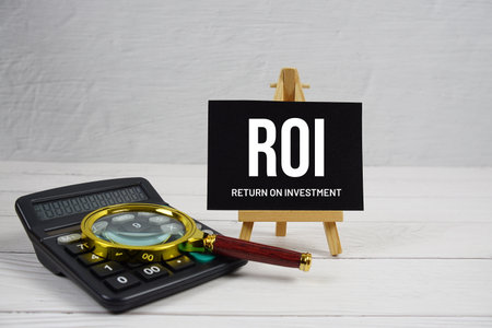 ROI abbreviation of Return On Investment text with magnifying glass and calculator on wooden backgroundの写真素材