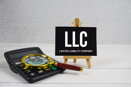 LLC abbreviation of Limited Liability Company text with magnifying glass and calculator on wooden...