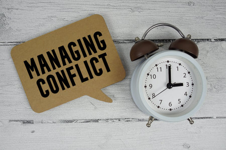 Managing conflict text with alarm clock on wooden background