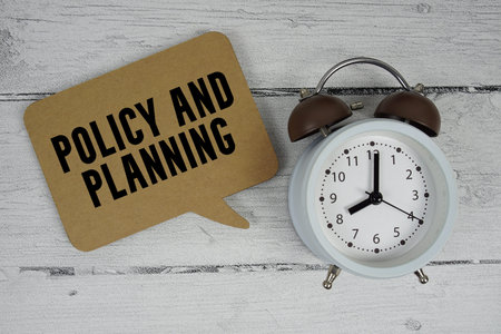 Policy and planning text with alarm clock on wooden background