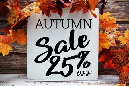 Autumn Sale 25% off text with maple leaf decoration on wooden background