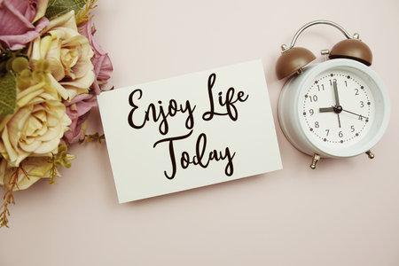 Enjoy Life Today text on paper card with alarm clock on pink backgroundの写真素材