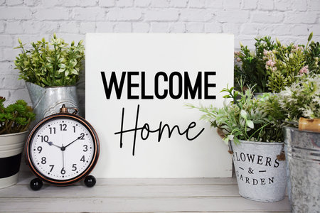 Welcome Home text with alarm clock on wooden background