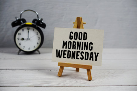 Good Morning Wednesday text with easel and alarm clock on wooden backgroundの写真素材