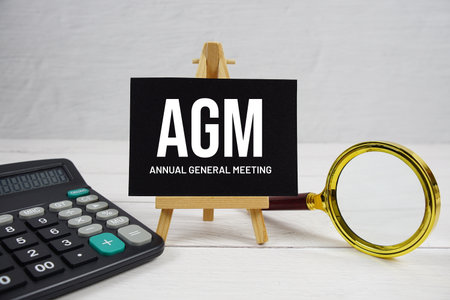 AGM abbreviation of Annual General Meeting text with magnifying glass and calculator on wooden backgroundの写真素材