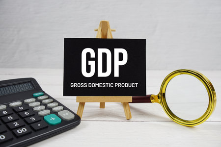 GDP abbreviation of Gross Domestic Product text with magnifying glass and calculator on wooden backgroundの写真素材