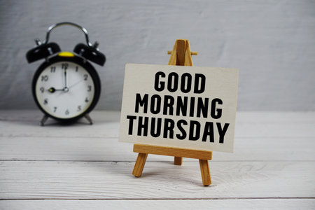 Good Morning Thursday text with easel and alarm clock on wooden backgroundの写真素材
