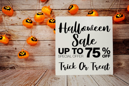 Halloween Sale 75% off text with LED pumpkin decoration on wooden background