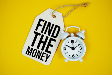 Find The Money text on price tag with alarm clock on yellow backgroundの写真素材