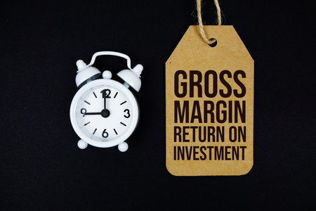 Gross Margin Return On Investment text on price tag with alarm clock on black backgroundの写真素材