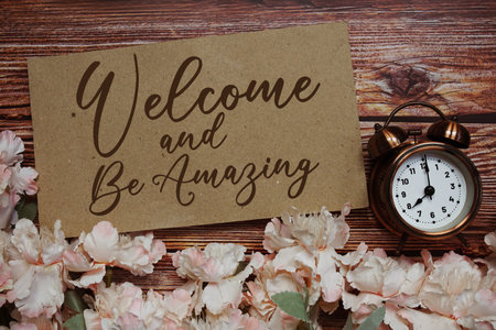 Welcome and Be Amazing text with alarm clock and flowers decoration on wooden backgroundの写真素材