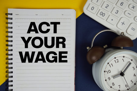 Act Your Wage text written on notepad with calculator and alarm clock on navy blue backgroundの写真素材