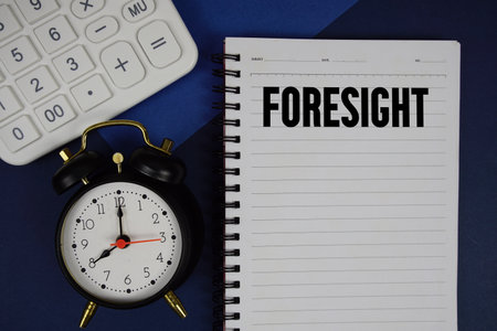 Foresight text written on notepad with calculator and alarm clock on navy blue backgroundの写真素材