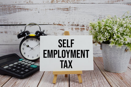 Self Employment Tax text with alarm clock and calculator on wooden backgroundの写真素材
