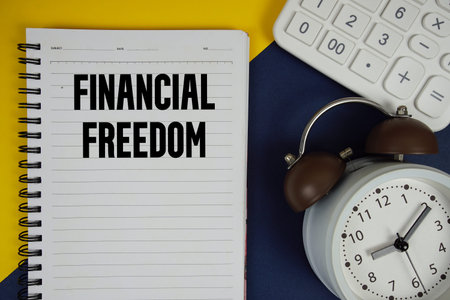 Financial Freedom text written on notepad with calculator and alarm clock on navy blue background