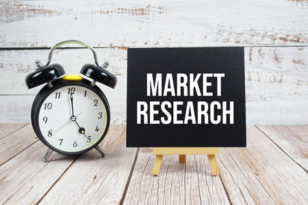Market Research text with easel and alarm clock on wooden background