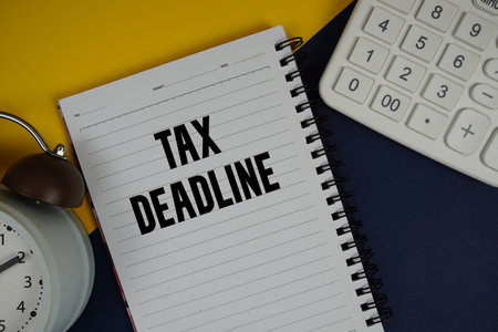 Tax Deadline text written on notepad with calculator and alarm clock on navy blue backgroundの写真素材