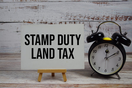 Stamp Duty Land Tax text with easel and alarm clock on wooden background