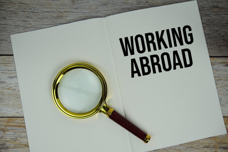 Working Abroad text message written on paper note with magnifying glass top view on wooden backgroundの写真素材