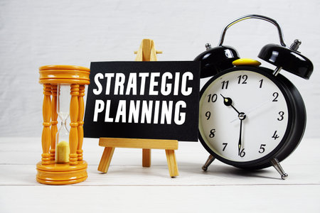 Strategic Planning text with hourglass and alarm clock on wooden background