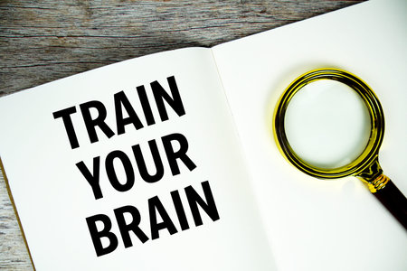 Train Your Brain text message written on paper note with magnifying glass top view on wooden...
