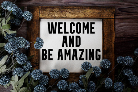 Welcome and Be Amazing text with flowers decoration on wooden background