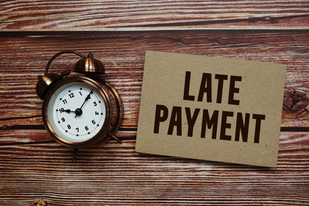 Late Payment text with alarm clock on wooden background