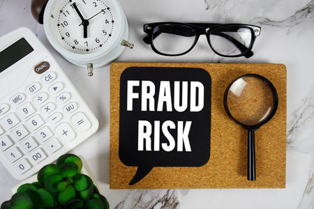 Fraud Risk text with Calculator, alarm clock and magnifying glass on marble background