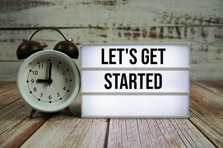 Let's Get Started text on light box with alarm clock on wooden background