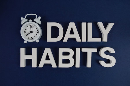 Daily Habits alphabet letters with alarm clock flat lay on blue background