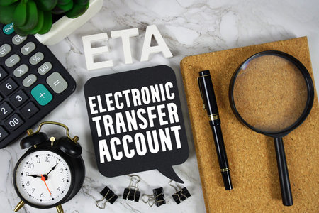 ETA Electronic Transfer Account text with Calculator, alarm clock and magnifying glass on marble...