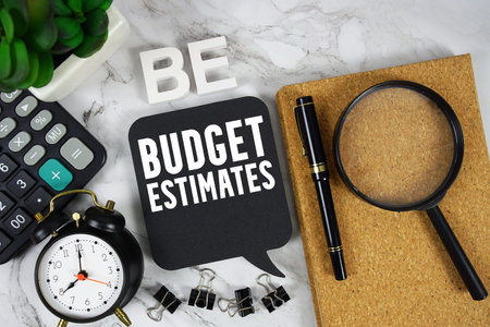 BE Budget Estimates text with Calculator, alarm clock and magnifying glass on marble background