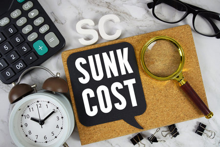 SC Sunk Cost text with Calculator, alarm clock and magnifying glass on marble background