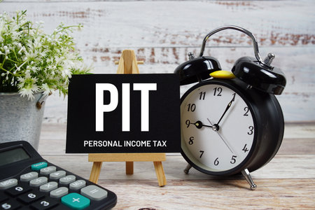 PIT Personal Income Tax text with alarm clock and calculator on wooden backgroundの写真素材
