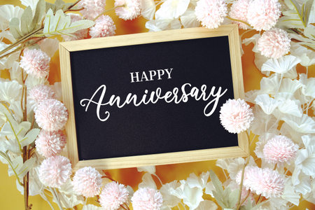 Happy Anniversaryy text with flowers decoration on yellow background