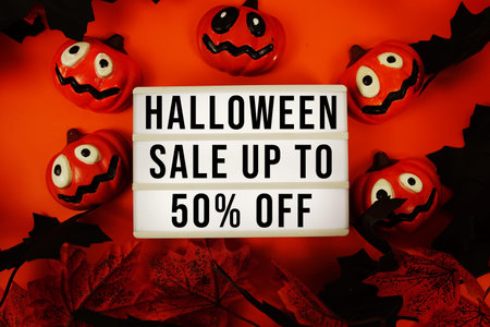 Halloween Sale up to 50% off text in light box with maple leaf decorations on orange background