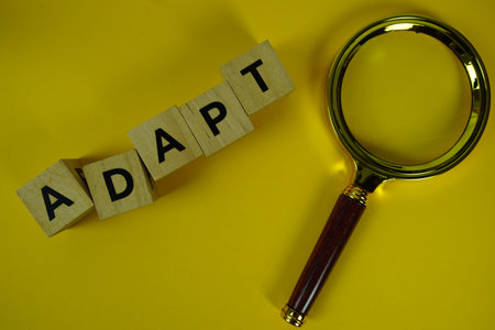 Adapt alphabet letters with magnifying glass flat lay on yellow background