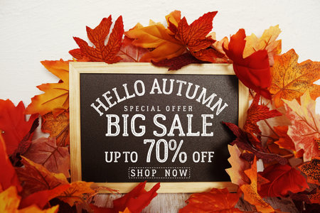 Hello Autumn Big Sale 70% text with maple leaf decoration on wooden background
