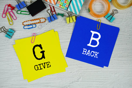 GB -  Give Back text on stick note with stationery on concrete background