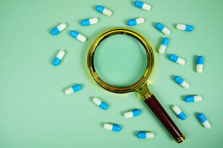 Medicine Capsule and magnifying glass on green background