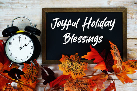 Joyful Holiday Blessings text written on chalkboard with alarm clock and maple leaf decoration on...