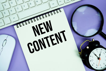 Notepad with the text "New Content" and white keyboard, wireless mouse, magnifying glass and alarm clockの写真素材