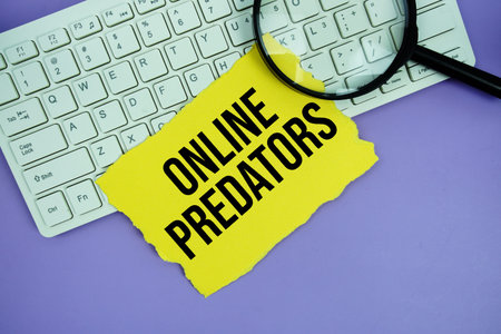 Yellow paper with text Online Predators and magnifying glass placed on a white keyboard